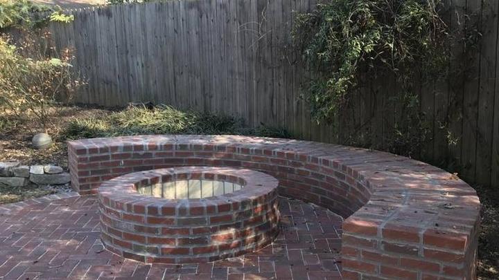 Round brick wood burning fire pit with a curved brick seating bench and back wall on a paver patio
