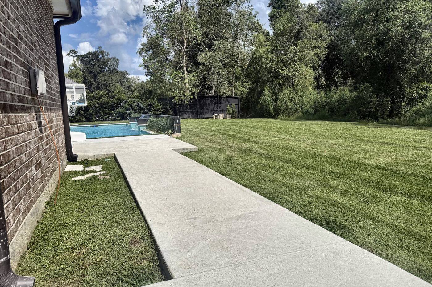 Broom finished concrete walkway running along the side of a brick house