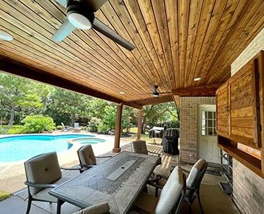 Covered patio with a stained cedar ceiling and fans, dining table set beneath it