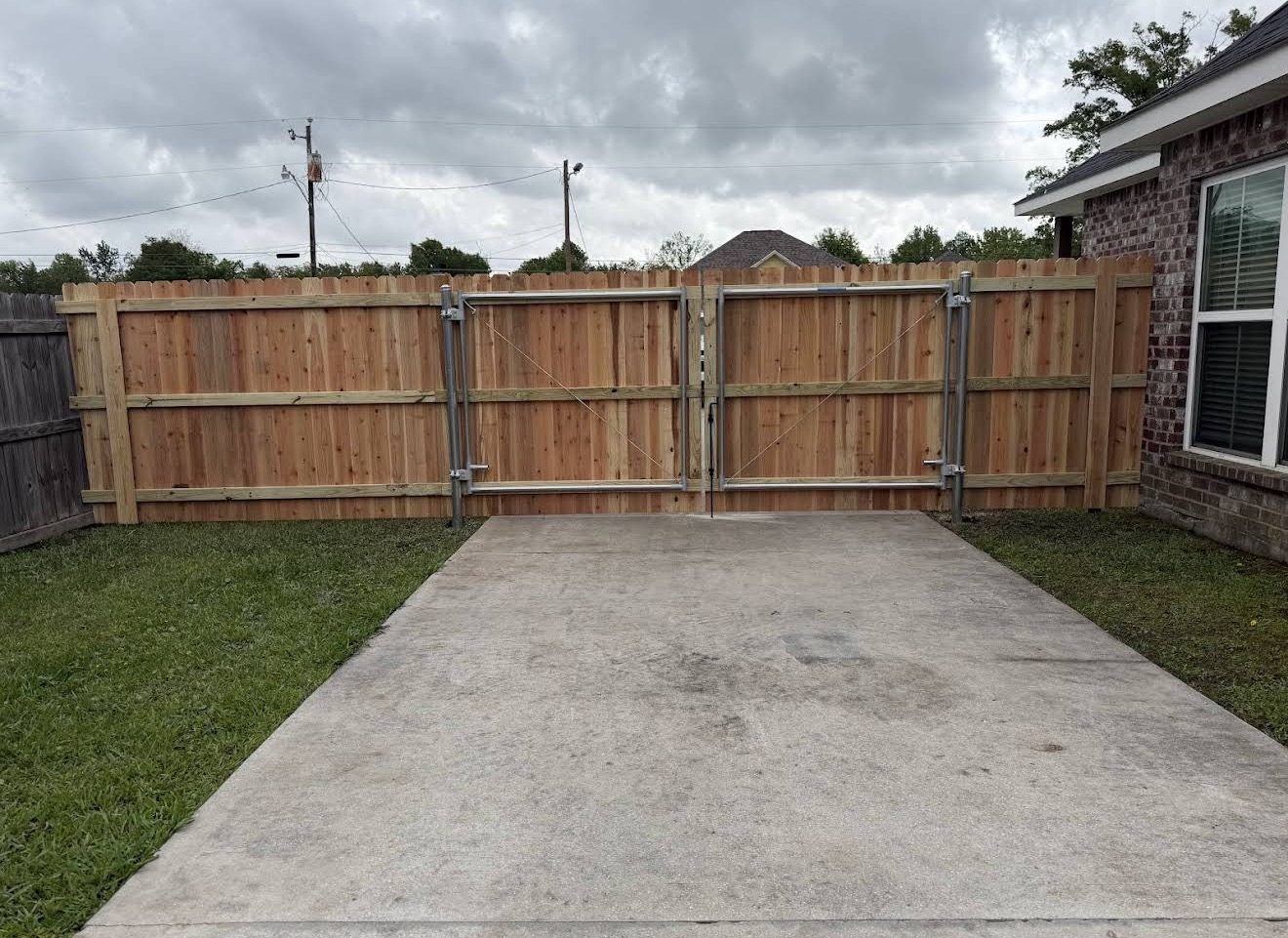Inside face of a cedar double drive gate showing the steel gate posts, welded metal gate frame and cable bracing that keep it square