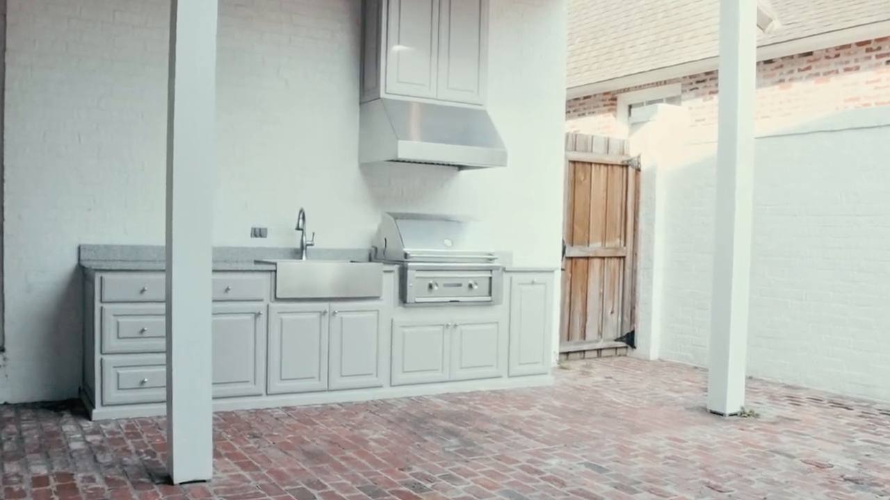 Built-in outdoor kitchen with a vent hood, farmhouse sink and gas grill under a covered patio